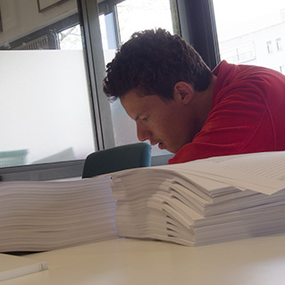 Een man werkt achter een hoge stapel papier. 