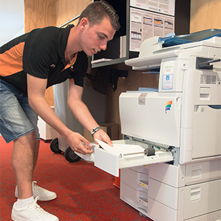 Een medewerker van de repro stopt papier in een printer. 